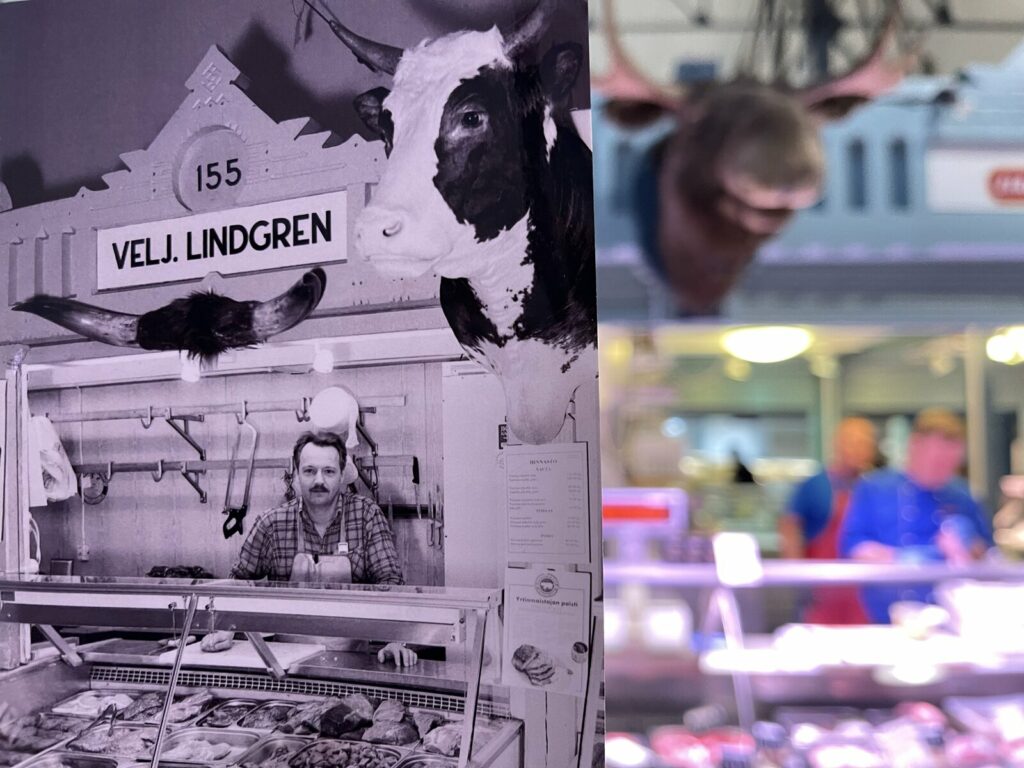Nykyisen Lihakipparien puodin edessä on mustavalkoinen valokuva, jossa Pekka Tuomela hymyilee ensimmäisen yrityksensä, Veljekset Lindgrenin lihatiskin takana.