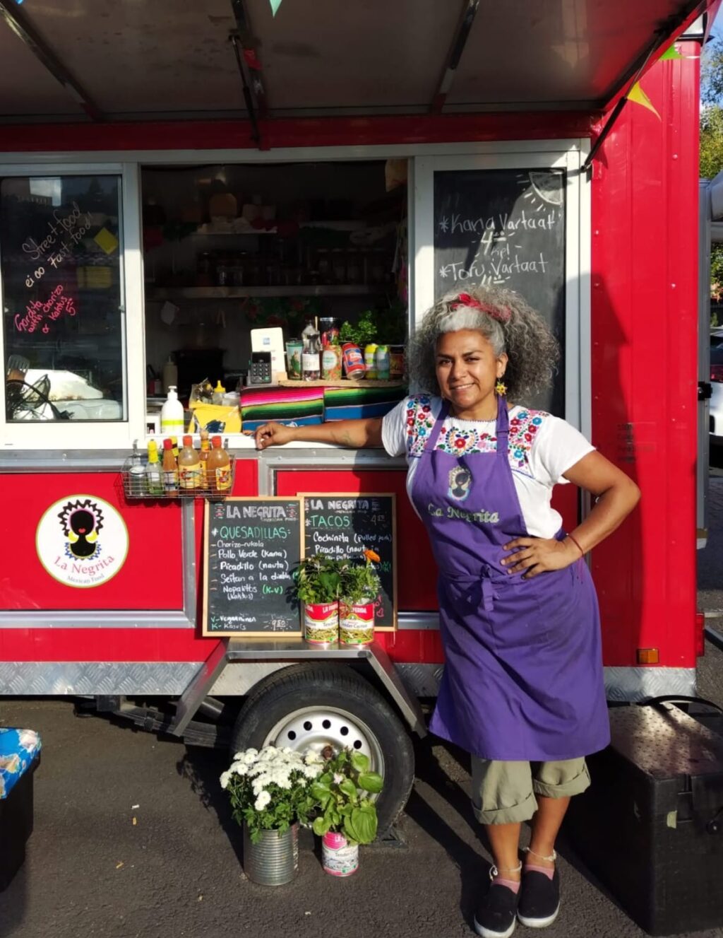 La Negritan yrittäjä Sol punaisen ruokakojunsa edessä Tammelantorilla kesäauringossa.