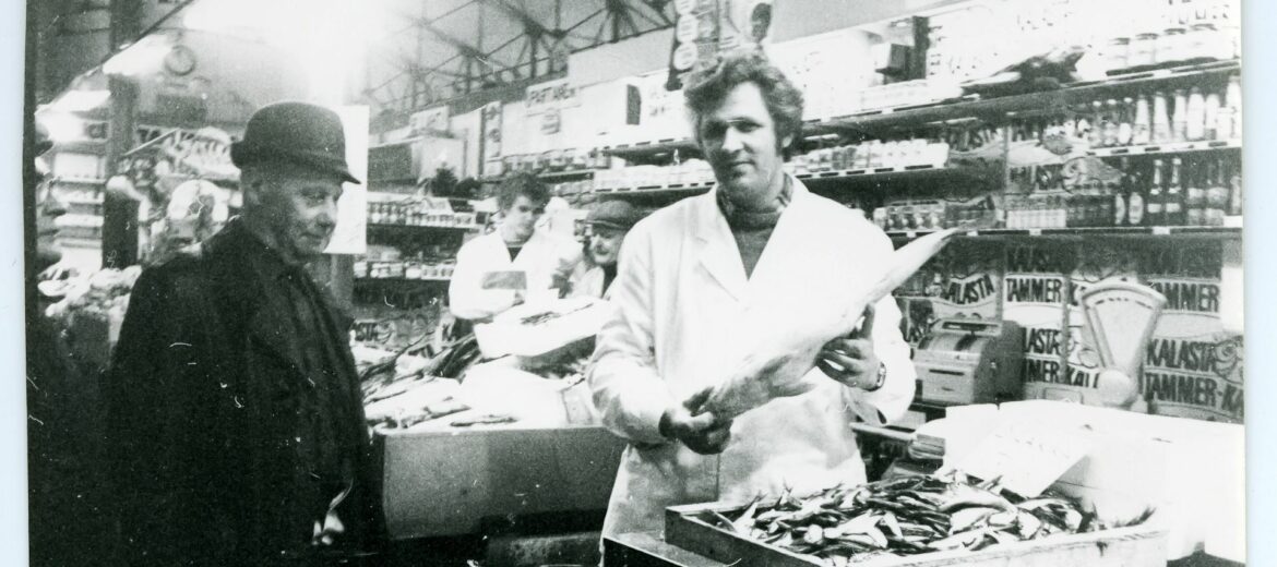 Mustavalkoisessa kuvassa Kalaherkkujen tiskillä kauppias Nygren esittelee kalaa asiakkaalle.