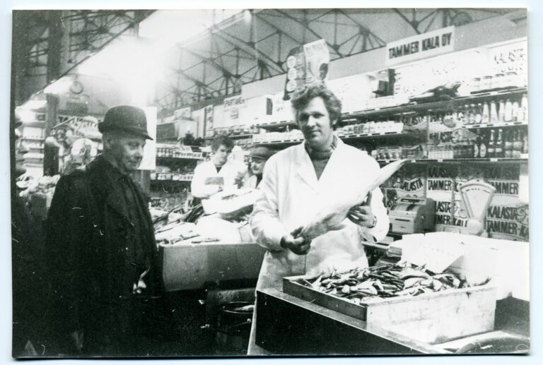 Mustavalkoisessa kuvassa Kalaherkkujen tiskillä kauppias Nygren esittelee kalaa asiakkaalle.